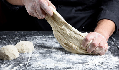 chef in black uniform kneads white wheat flour dough