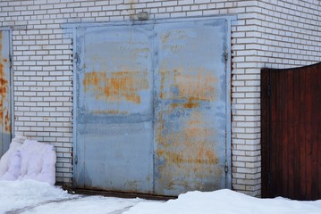 gray and rusty metal gates on a brick facade of a garage in white snow