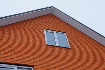 part of the red brick wall of the house with a white window against the sky