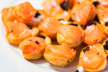 Delicious profiteroles with black caviar and salmon on a plate close-up