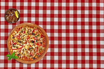 Whole round supreme pizza with coke or cola glass on red tablecloth from top view 