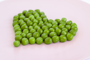 Green peas heart shaped, pink plate on white table. St. Valentine's day concept