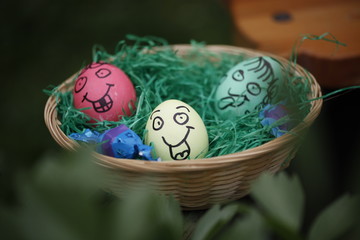 Osterkorb mit bunten Eiern in Rot, Grün und Gelb und angemalten, lachenden Gesichtern