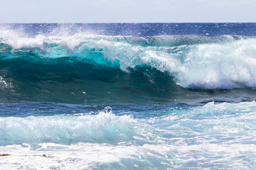 Wave breaking near shore on South Point, on Hawaii's Big Island. Sea foam in foreground. Foam on top of wave's clear blue-green water; deep blue Pacific ocean in the background.  