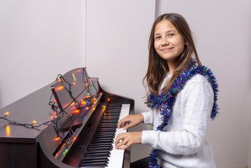 Young girl child plays piano. There are lights on the piano.