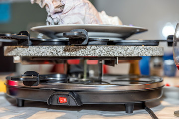 traditional swiss electric raclette stone grill unit with individual skillets on christmas table