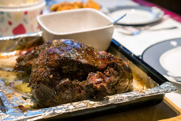 A roast leg of lamb on baking tray on christmas table