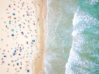 Fototapeta na wymiar An aerial view of people on the beach with blue water on hot summer's day
