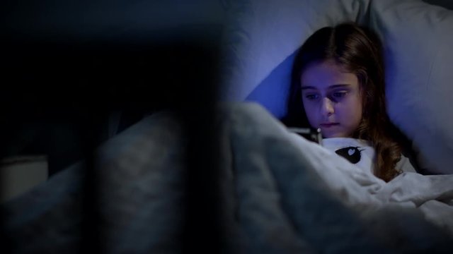 8 Year old girl in bed at night watching a movie on her tablet. Camera tracking left and right.