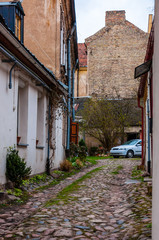 Fototapeta na wymiar Arch gates to medieval paving stone grungy but stylish and cozy end street with parked car in Old Town of Vilnius. Classical European architecture street design