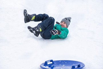 Fototapeta na wymiar Boy falls rolling down a hill on snow saucer. Winter games