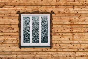 White wooden window in the wall of raw brown wooden planks with knots. Frontal view. Close-up.