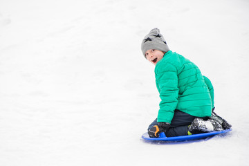 Fototapeta na wymiar Happy laughing boy slides down the hill on snow saucer. Seasonal concept. Winter day