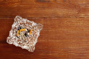 top view of cigarette butts in a glass ashtray on a wooden background with copy space