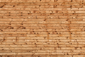 Wall made of rough brown wooden planks with knots. Frontal view. Close-up.