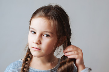Fototapeta premium Little serious beautiful girl braids a pigtail from a long hair portrait