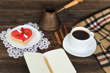 Cup of coffee, heart shaped cookies with message, notebook, pencil and coffee pots on a brown wooden table