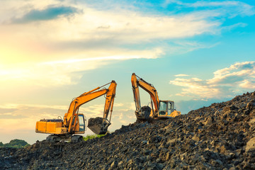 Two excavators work on construction site at sunset