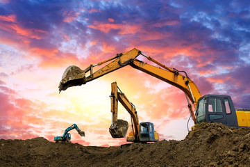 Three excavators work on construction site at sunset