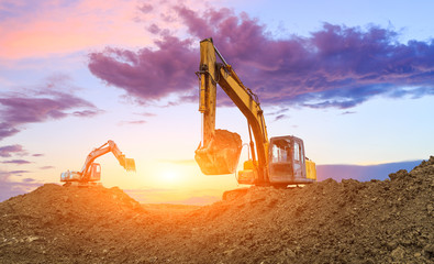 Two excavators work on construction site at sunset
