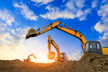 Three excavators work on construction site at sunset