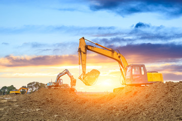 Three excavators work on construction site at sunset