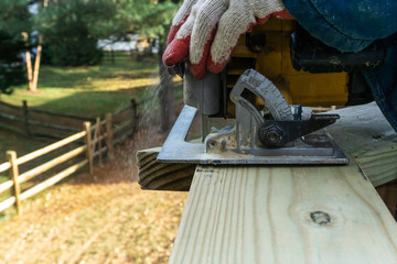 handyman works with circular saw on wooden toprail