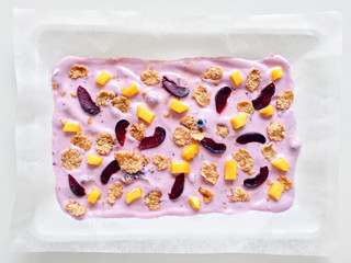 Homemade healthy frozen cereal blueberry yogurt bark with mango and cherry on a white background,...