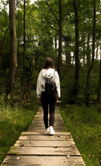 Girl walking on a pathway in the forest / Girl walking in the forest photographed from behind / girl with beautiful backpack in the forest
