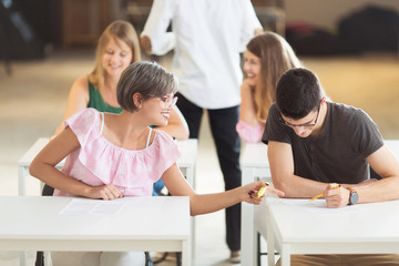 Young students sitting together and having exam in classroom