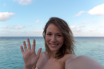Fototapeta na wymiar cheerful young woman in honeymoon greeting her friend. Sea as Background