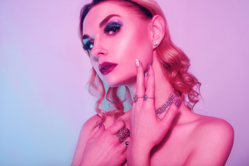 Naklejka premium Beautiful woman in a necklace, earrings and ring. Model in jewelry, diamonds. Fashion neon portrait of young beautiful girl with jewelry. Blond girl with cerly hair and red lips. Perfect make-up. 