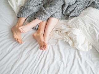 Close up of the feet of a couple on the bed. Loving couple is lying on bed under blanket. Love and relationships concept.
