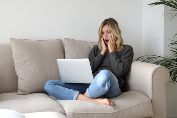 Frau sitzt auf einem Sofa und schaut erschrocken auf einen Laptop