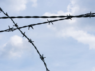 Close-up of crossed barbed wire against cloudy blue sky - security, isolated design element