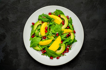 salad with avocado, arugula, spinach, pomegranate, seeds on a concrete background