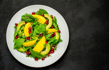 salad with avocado, arugula, spinach, pomegranate, seeds on a concrete background