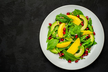 salad with avocado, arugula, spinach, pomegranate, seeds on a concrete background