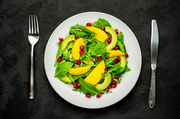 salad with avocado, arugula, spinach, pomegranate, seeds on a concrete background