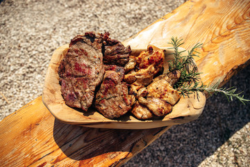 Delicious grilled pork and chicken meat with rosemary on the traditional wooden dish near the barbecue fireplace