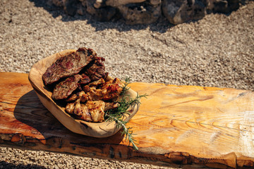 Delicious grilled pork meat with rosemary on the traditional wooden dish near the barbecue fireplace