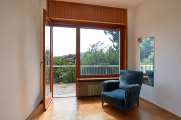 Room interior with open window and blue velvet armchair in country house