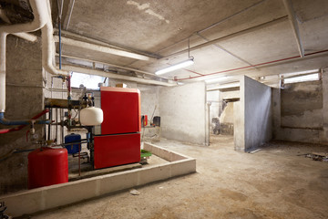 Basement with red heating boiler and dirty floor in old house interior