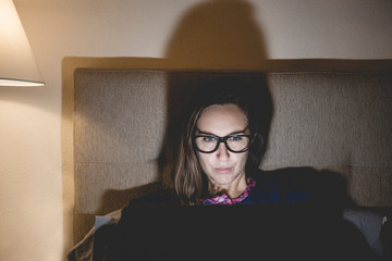 Pajama woman in bed at home bedroom working concentrated with the laptop at night or using the internet social network chat in the concept of dependence on technology