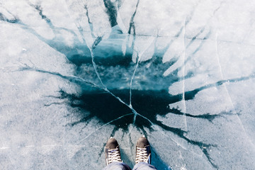 Skater in black skate boots in front of spot of fairy blue clear lake ice with cracks as part of holiday vacation winter activity