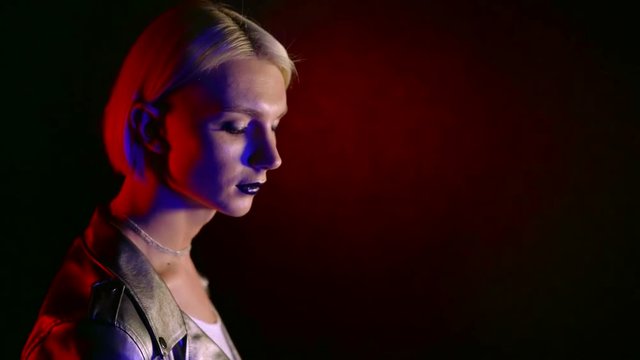 close-up portrait of a cute male bisexual blonde with black lipstick on her lips in a dark room in the light of blue and red neon