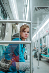 Young beautiful girl with brown hairs and bright make up, dressed in blue coat, black hoodie,...