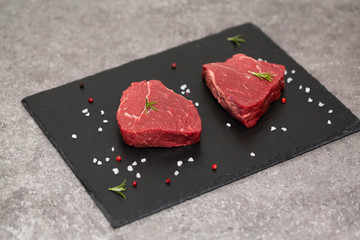Raw beef steak and spices on slate board. Raw meat on black background. Top view. Copy space