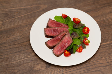 Juicy steak medium rare beef with green salad and tomatoes on white plate