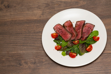 Juicy steak medium rare beef with green salad and tomatoes on white plate